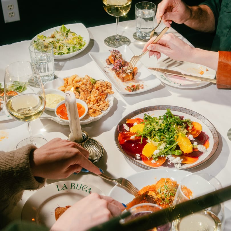 Diners enjoying various Italian dishes and white wine at a candlelit table at La Buca.