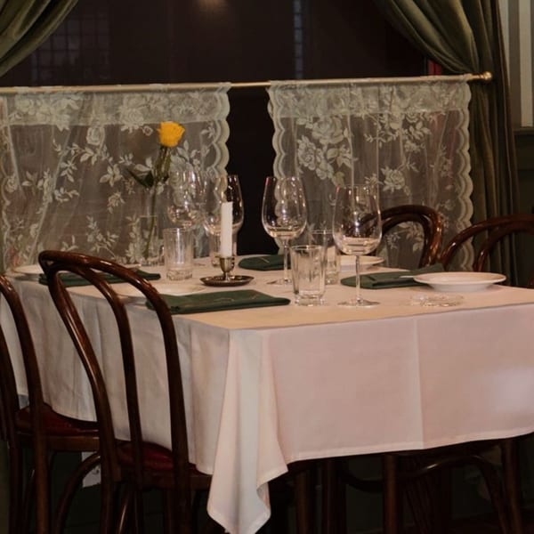 A dining table set with white tablecloth, green napkins, wine glasses, and a single yellow rose.