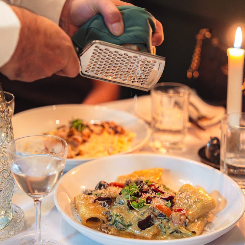 A chef grates cheese over a plate of creamy pasta with vegetables at La Buca.