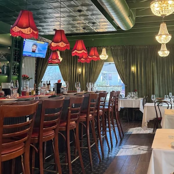 A restaurant interior with a bar, red lampshades, green curtains, and dining tables.
