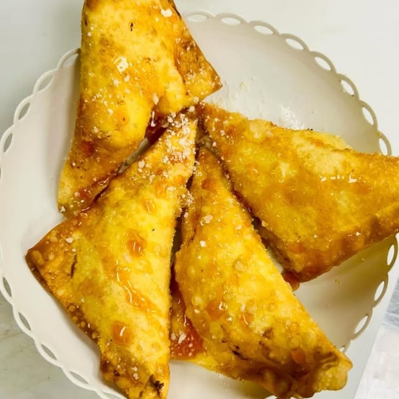 Golden-fried Italian pastries, drizzled with honey and sprinkled with powdered sugar, in a white scalloped bowl.
